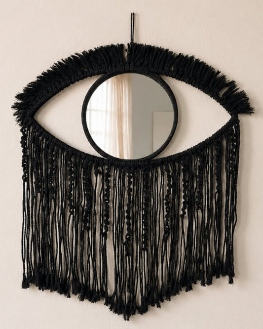 Black fringe mirror shaped like an eye on a beige wall