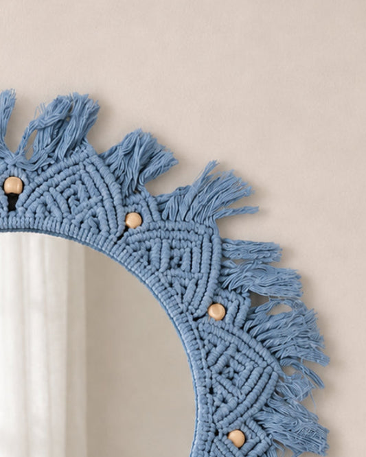 Round blue macrame mirror with tassels on a beige wall
